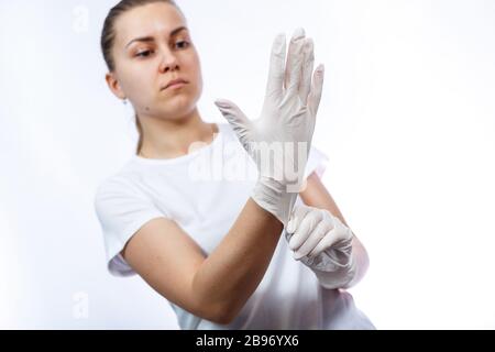 Fille paramédic met des gants médicaux blancs sur les mains. Protection contre les germes et les virus. Elle est dans un T-shirt blanc sur un fond blanc. Banque D'Images