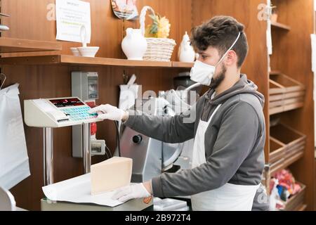 Avetrana, Italie, - 19 mars 2020. Le vendeur sert un costeumer un fromage, portant un masque médical et des gants de protection pendant l'épidième de Coronavirus. Sho Banque D'Images