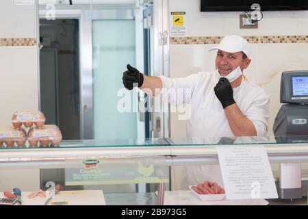 Avetrana, Italie, - 19 mars 2020. Le vendeur sert une viande plus chère, portant un masque médical et des gants de protection pendant l'épidième de Coronavirus. SHOPP Banque D'Images