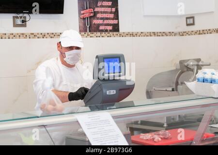 Avetrana, Italie, - 19 mars 2020. Le vendeur sert une viande plus chère, portant un masque médical et des gants de protection pendant l'épidième de Coronavirus. SHOPP Banque D'Images