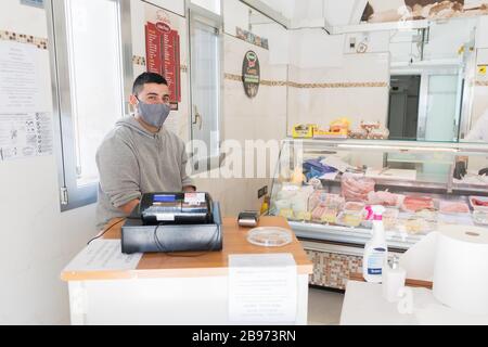 Avetrana, Italie, - 19 mars 2020. Le vendeur sert une viande plus chère, portant un masque médical et des gants de protection pendant l'épidième de Coronavirus. SHOPP Banque D'Images