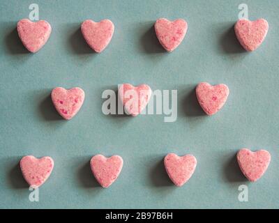 Groupe de bonbons roses en forme de coeur disposés en motif géométrique sur le fond bleu. Symbole d'amour. Couleurs pastel. Texture clairement définie. Banque D'Images