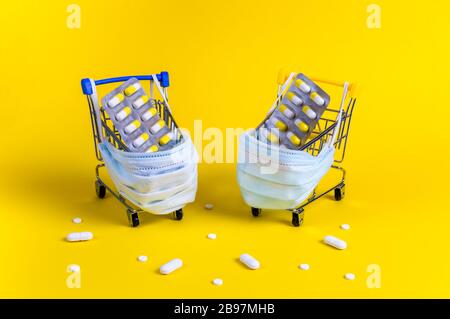 Deux chariots à provisions avec blister et masques médicaux pour la protection contre les virus et les pilules blanches sur fond jaune. Concept créatif de sho en ligne sûr Banque D'Images