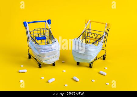 Deux chariots avec masques médicaux pour la protection contre les virus entourés de pilules blanches sur fond jaune. Concept créatif de shopping en ligne sûr Banque D'Images