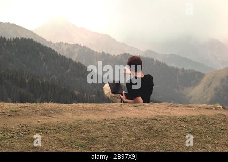 Jeune homme indépendant couché et travaillant avec un ordinateur portable en montagne Banque D'Images