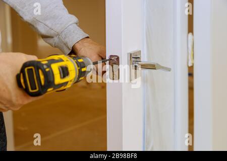 Le travailleur assemble la serrure dans la porte en bois de la nouvelle maison Banque D'Images