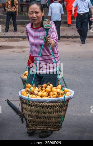 Chongqing, Chine - 9 mai 2010 : centre-ville. Femme en chemise rose porte 2 grands paniers chacun sur le côté de l'épaule pole. Rempli de fruits jaune-orange. Banque D'Images