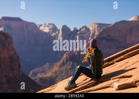 Femme aux cheveux rouges assise sur la falaise surplombant le parc national de Zion Banque D'Images
