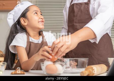 La mère et la fille aident à recueillir des œufs dans des tasses claires placées sur la table pour cuisiner. Sélectionner la profondeur de champ faible focale de mise au point. Banque D'Images