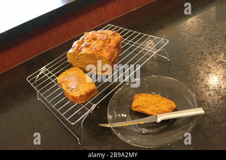 Tranches de pain de citrouille frais maison coupé de pain de citrouille avec couteau, sur plaque transparente et grille de refroidissement sur comptoir noir Banque D'Images