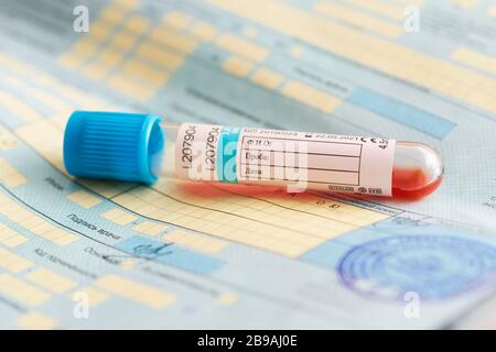 Un tube à essai avec un test sanguin sur un document d'hôpital. Traduction en russe : nom complet, échantillon de sang, date, signature du médecin. Banque D'Images