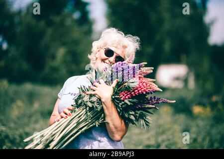 Blonde femme mûre tenant un bouquet de lupin sur le fond de la nature. Le concept de beauté et de corps positif. Coucher de soleil Banque D'Images