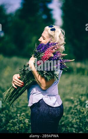 Blonde femme mûre tenant un bouquet de lupin sur le fond de la nature. Le concept de beauté et de corps positif. Coucher de soleil Banque D'Images