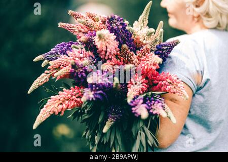 Blonde femme mûre tenant un bouquet de lupin sur le fond de la nature. Le concept de beauté et de corps positif. Coucher de soleil Banque D'Images