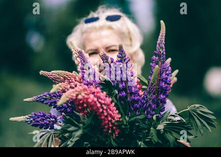 Blonde femme mûre tenant un bouquet de lupin sur le fond de la nature. Le concept de beauté et de corps positif. Coucher de soleil Banque D'Images