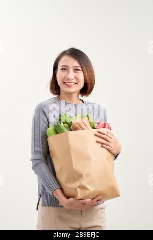 Belle jeune femme dans un tablier tenant le sac de shopping en papier plein de légumes frais et souriant Banque D'Images