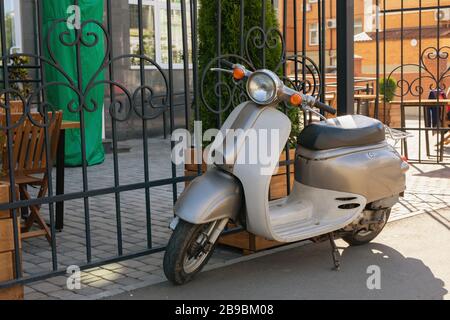 Scooter blanc et métallique garé près de la clôture en fer forgé de la rue de la ville en été ensoleillé midi. Kazan, Russie, 08.07.2019 Banque D'Images