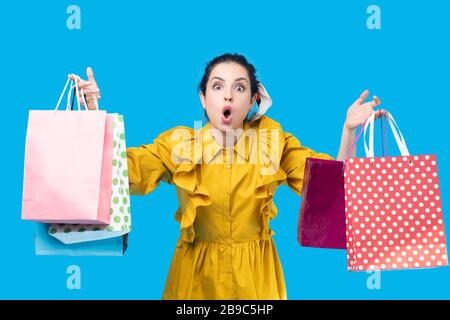 Jeune femme dans une robe à la moutarde tenant des sacs à provisions et regardant surpris Banque D'Images