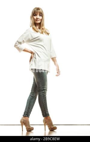 La mode. Jeune femme blonde pantalon denim blanc bat sleeve top High heels. Modèle féminin posant en pleine longueur isolée Banque D'Images