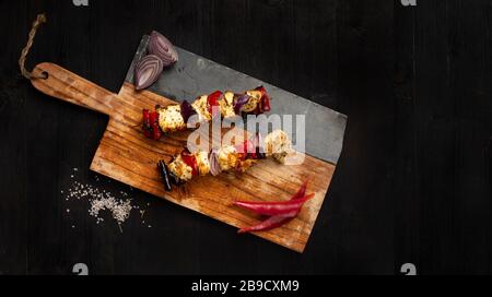 Savoureux brochette de poulet et de légumes avec oignon et poivre de côté, isolée sur fond en bois sombre. Espace pour le texte à gauche. Photogr. Produit contraste haute lumière Banque D'Images