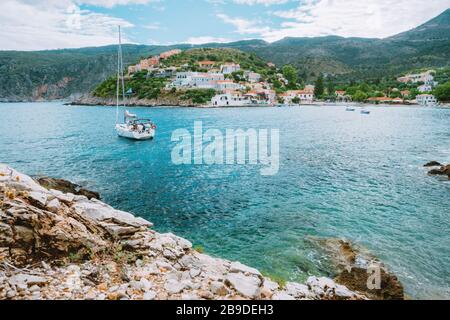 Assos jolie ville, sur l'île de Céphalonie, Grèce. Vue sur la magnifique baie avec bateau à voile et montagnes en arrière-plan. Banque D'Images