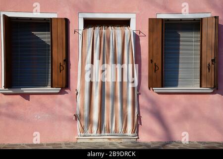 Fermez la porte d'entrée et deux fenêtres avec volets de maison rose pâle à Burano Banque D'Images