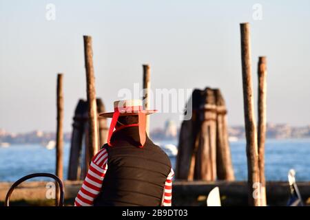 Gondolier avec chapeau et chemise à rayures rouge-blanc pour se reposer sur la lagune de Venise à partir d'une chaise Banque D'Images