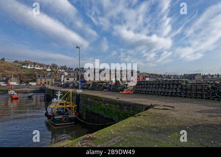 Des pots de crabe et de homard empilés avec Buoys ligne le Breakwater et Quay of Gourdons Inner Harbour avec le village de pêche en arrière-plan. Banque D'Images