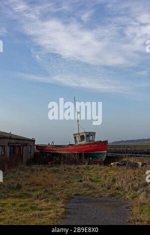 Un vieux bateau de pêche traditionnel en bois à quelques pâtés de maisons et hors de l'eau dans une petite rue latérale à côté de la brise-lames du port. Banque D'Images