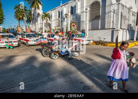 Maya femme vendant des métiers devant des taxis décorés avant la procession, Festival de notre Dame de Guadalupe, rue à Catemaco, Veracruz, Mexique Banque D'Images