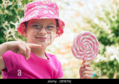 Petite fille dans un chapeau rose tenant grand lollipop Banque D'Images