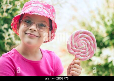 Petite fille dans un chapeau rose tenant grand lollipop Banque D'Images