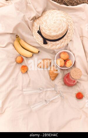 Pique-nique en plein air sur le terrain, une journée ensoleillée avec croissant, banane, fruits et une bouteille de boisson rouge. Banque D'Images