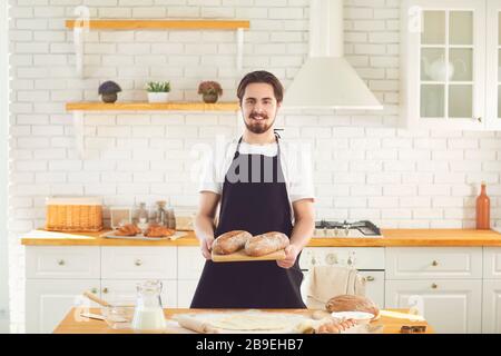 L'homme barbu de Baker tient dans ses mains du pain frais debout dans la cuisine. Banque D'Images