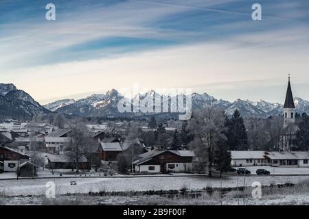 Vue aérienne de la petite ville allemande confortable au fond de la montagne au lever du soleil en hiver, Halblech, Allemagne, Bavière, branches d'arbres sont Banque D'Images