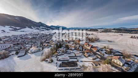 Vue aérienne de la petite ville allemande confortable au fond de la montagne au lever du soleil en hiver, Halblech, Allemagne, Bavière, branches d'arbres sont Banque D'Images