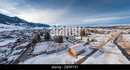 Vue aérienne de la petite ville allemande confortable au fond de la montagne au lever du soleil en hiver, Halblech, Allemagne, Bavière, branches d'arbres sont Banque D'Images