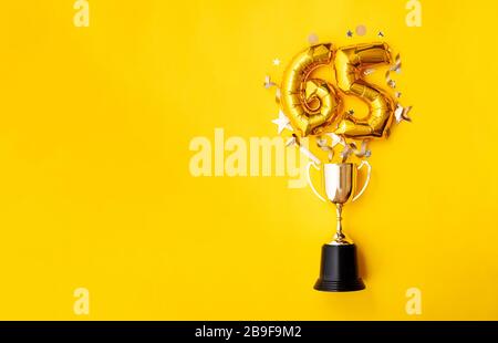 Ballon de célébration du numéro 65 Gold anniversaire explosant à partir d'un trophée gagnant Banque D'Images