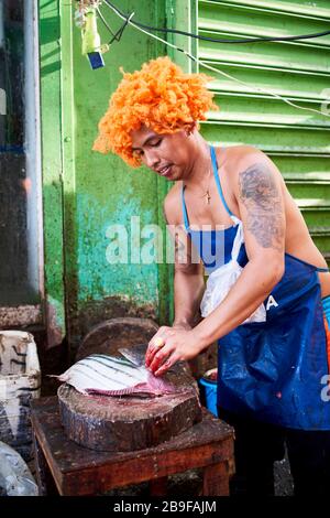 Poissonnier avec une perruque d'orange drôle vendant des poissons dans les rues du marché public du carbone. Banque D'Images