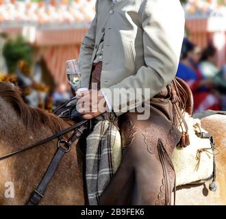 Pilote à cheval vêtu d'un costume traditionnel et tenant un verre de sherry de fino (manzanilla sherry) à la foire d'avril (Feria de Abril), Séville Fai Banque D'Images