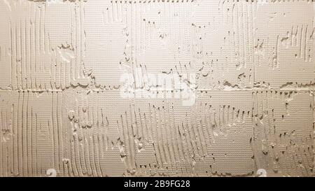 Colle pour une tuile avec un modèle d'engrenage. Installation de tuiles. La surface du mur est recouverte de pâte adhésive avant de poser des tuiles ou des s décoratifs Banque D'Images