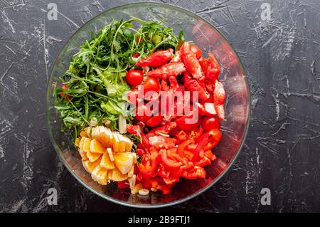 Salade fraîche composée de viande de crabe, de poivron, de tomate cerise, d'orange, d'arugula et d'huile d'olive dans un bol en verre sur fond noir Banque D'Images