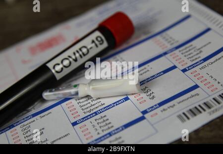 Viersen, Allemagne - 22 mars. 2020: Gros plan du tube d'échantillon de sang isolé avec le mot covid-19 et l'ampoule de verre de médicament blanc. Demande de test de laboratoire floue Banque D'Images