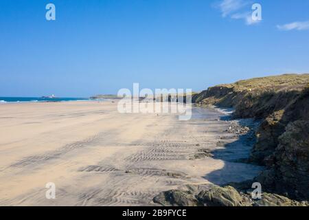 Photo aérienne d'une plage de Gwithian vide avec vagues briser et phare de rêve en arrière-plan et dunes de sable sur la droite sur une journée de ciel bleu Banque D'Images