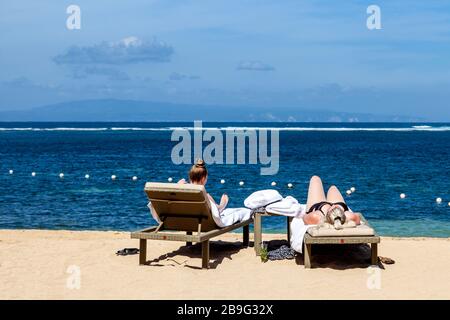 Deux visiteurs bronzer sur la plage, Sanur Beach, Sanur, Bali, Indonésie. Banque D'Images