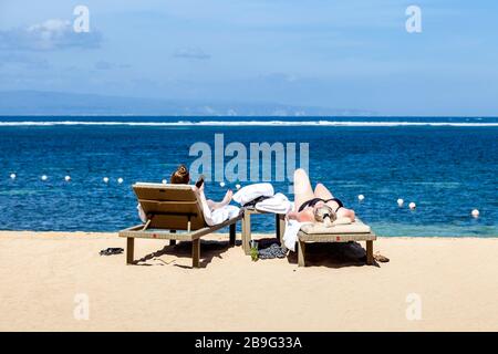 Deux visiteurs bronzer sur la plage, Sanur Beach, Sanur, Bali, Indonésie. Banque D'Images