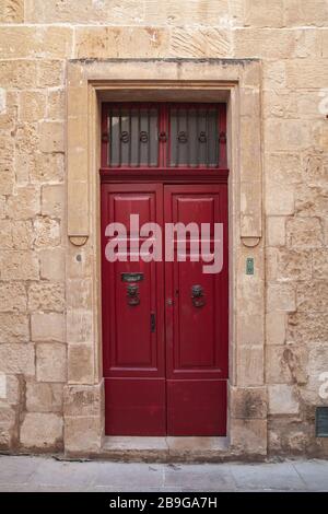 Porte en bois rouge vintage dans un mur en pierre jaune. Mdina, vieille ville fortifiée dans la région du Nord de Malte Banque D'Images