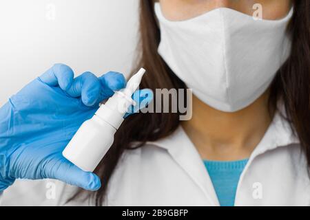 Une femme qui utilise un spray pour le traitement de la grippe ou le nez courant conserve des médicaments dans la main. Le médecin dans le masque de protection et les gants bleus montre un jet de nez pendant Banque D'Images