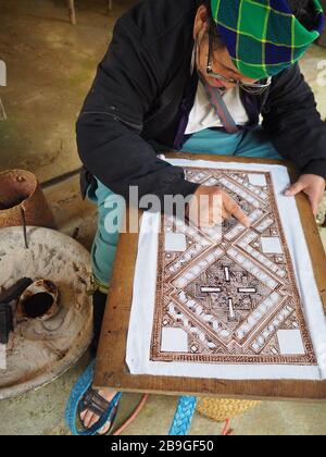 Une femme Hmong utilisant des modèles traditionnels pour peindre sur du tissu à Sapa, au Vietnam, qu'elle fera ensuite dans des sacs et d'autres objets d'artisanat Banque D'Images