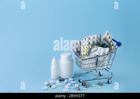 Diverses capsules, comprimés et médicaments dans le chariot de boutique et pilules débordant de la bouteille blanche sur fond bleu. Achat et shopping concept de médecine. Banque D'Images